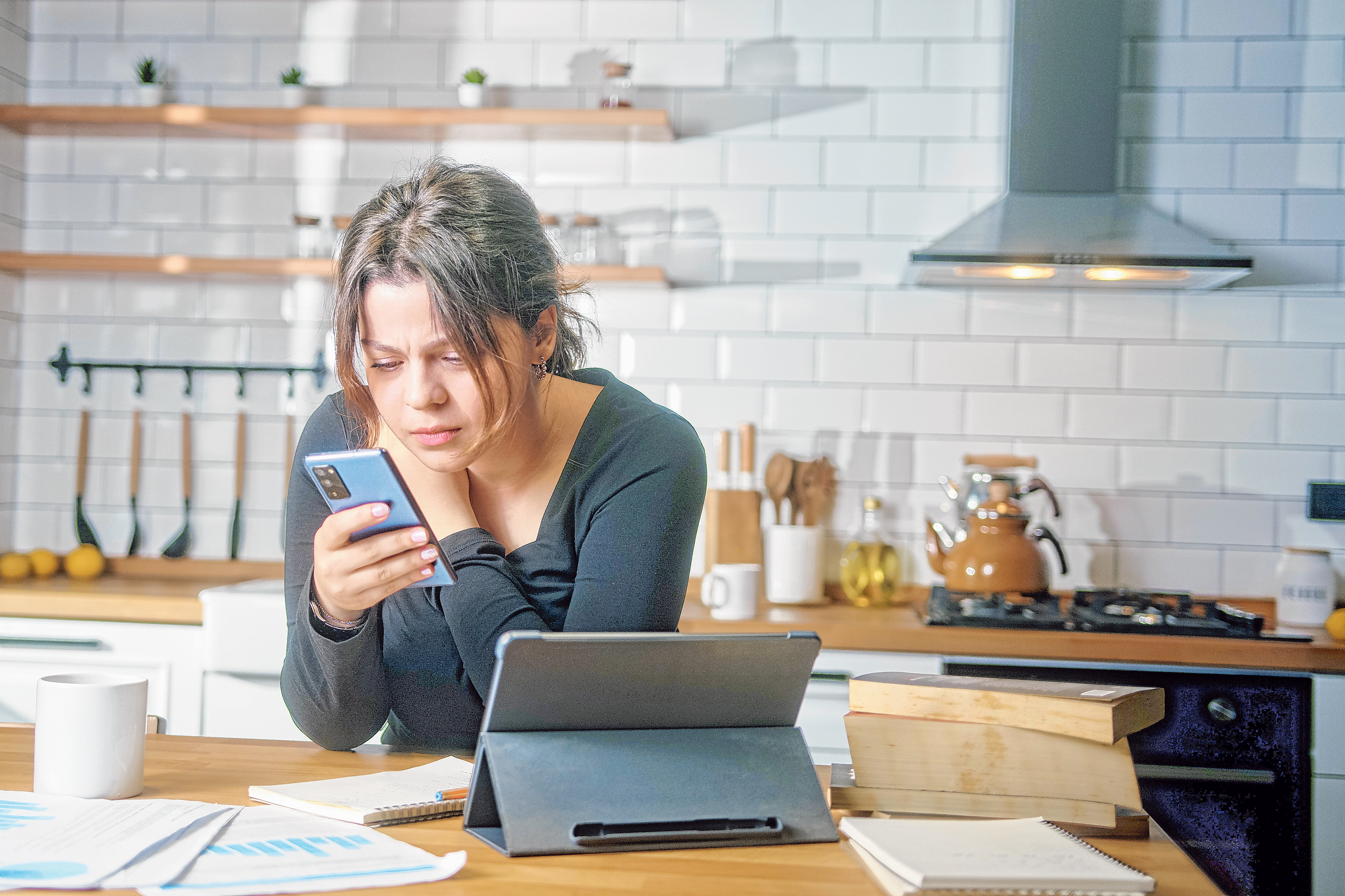 Eine junge Frau sitzt in der K&uuml;che und informiert sich per Smartphone.
