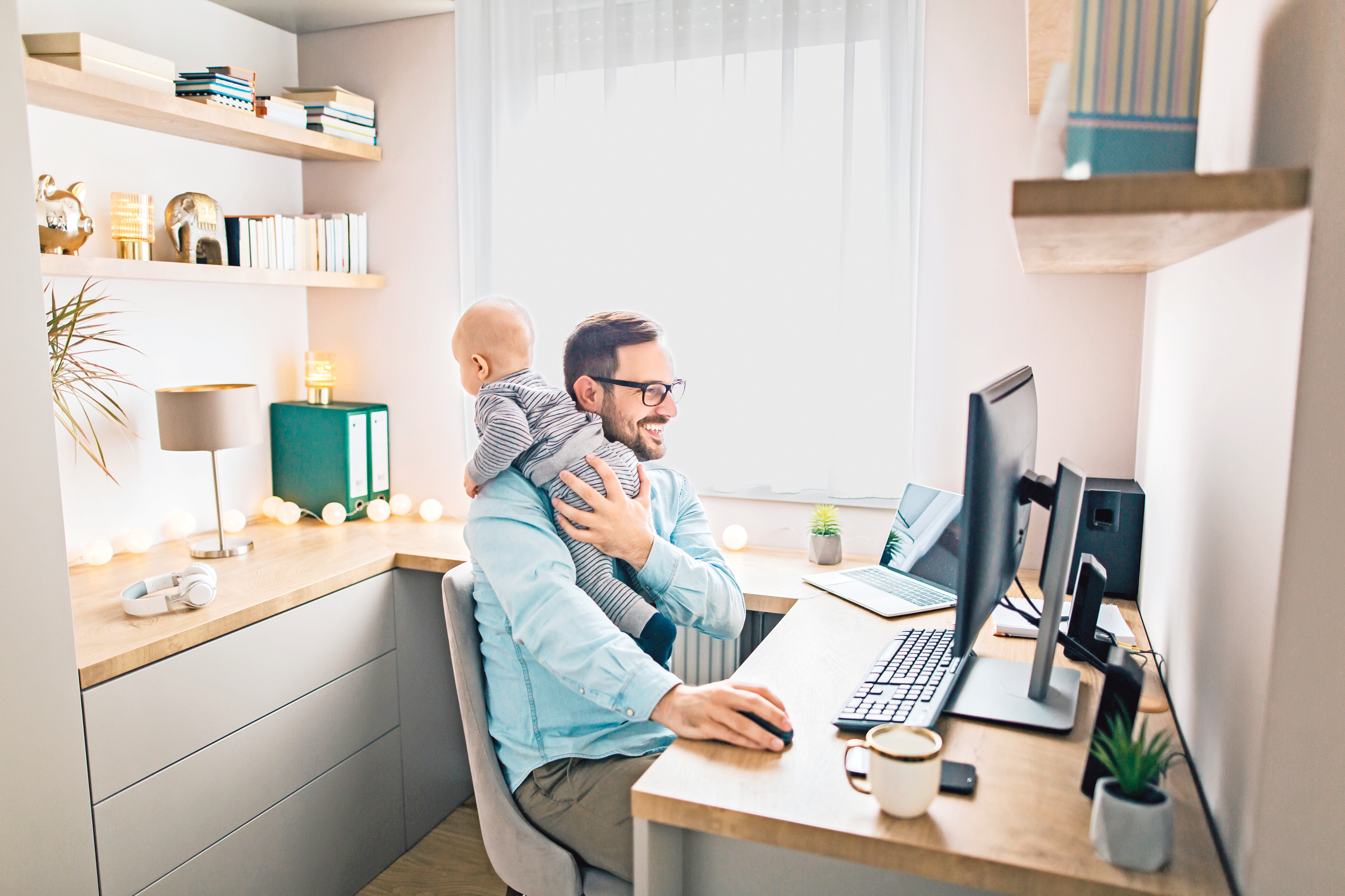 Ein Mann arbeitet am Computer mit Baby auf der Schulter.
