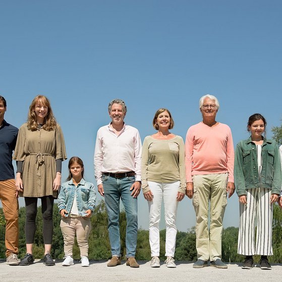 Menschen verschiedenen Alters, mit und ohne Behinderung, stehen l&auml;chelnd nebeneinander.